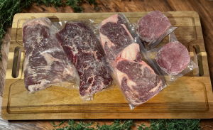 flank steak, tri tip, rib eyes and hamburger patties on a cutting board